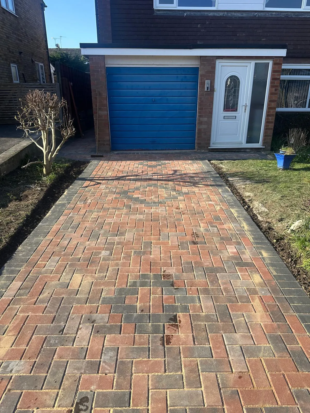 Red and charcoal block paved driveway to a blue garage