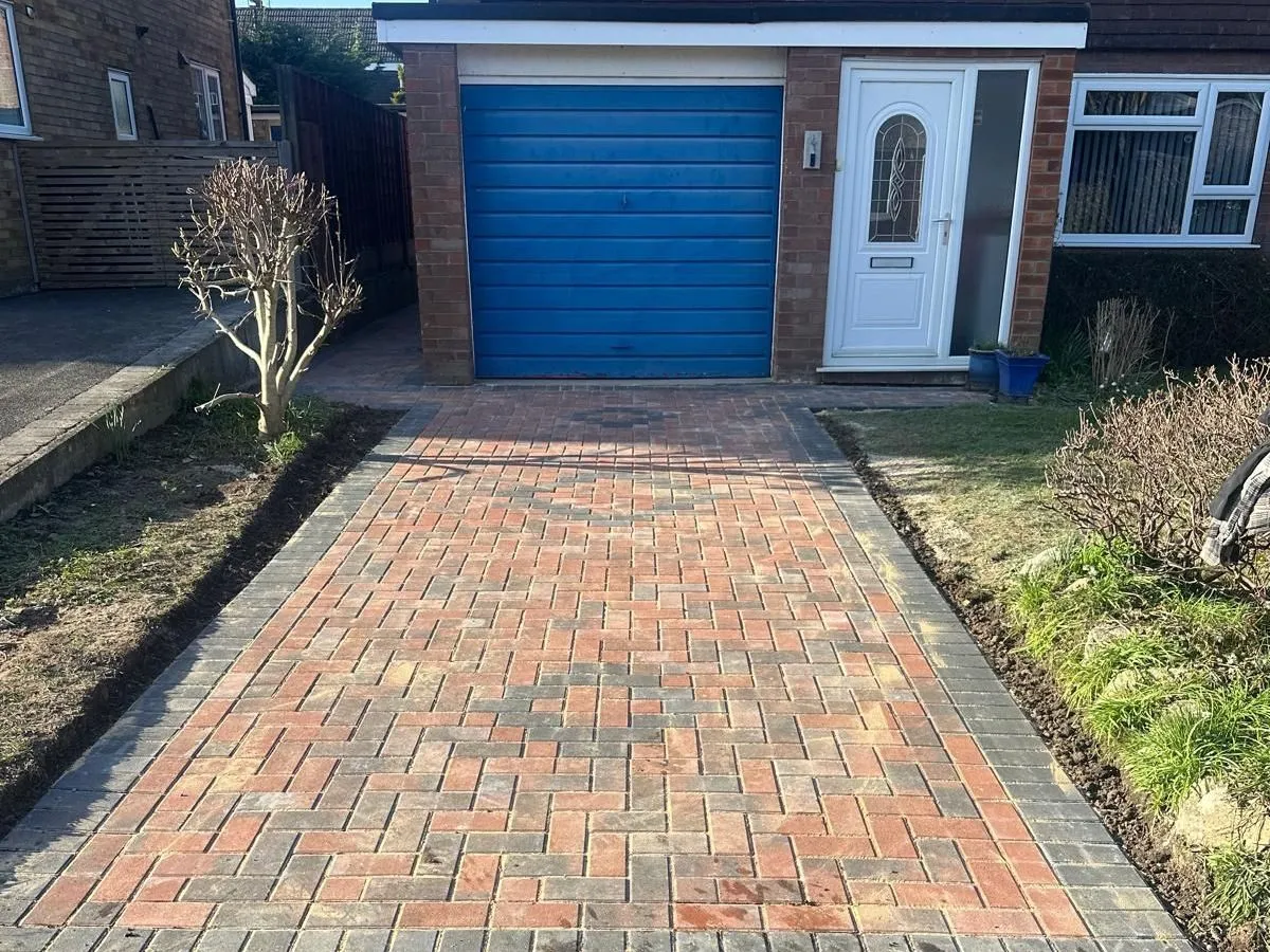 New red and charcoal herringbone block paved driveway leading to a blue garage door in Manchester
