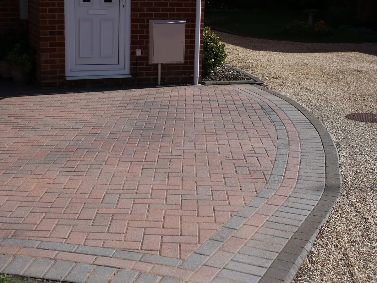 Curved red herringbone block paved driveway with a charcoal border edged by gravel