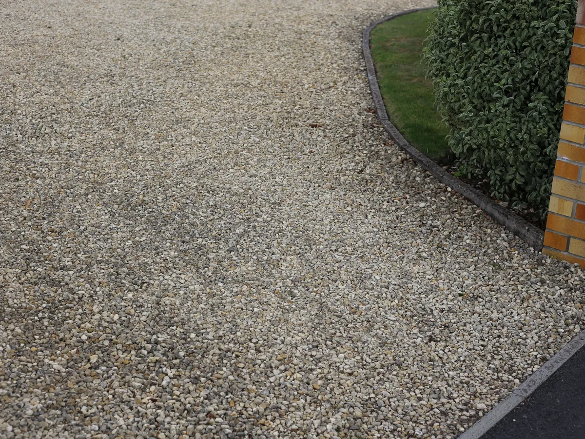 Buff gravel driveway curving beside a lawn