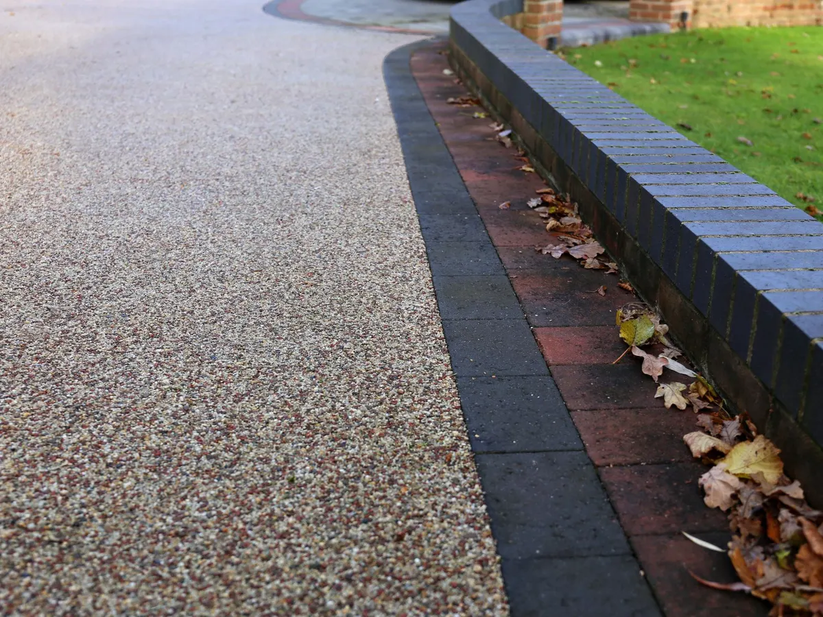 Resin bound surface edged with blocks beside a low wall and lawn